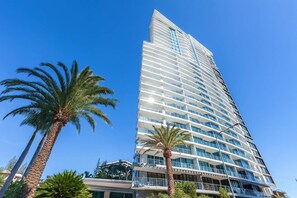 A tall hotel with multiple balconies, palm trees, and a clear blue sky. - Modern 2-Bedroom Oasis with Pool (Surfers Paradise)