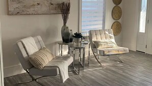 Een moderne woonkamer met twee leren fauteuils, een glazen salontafel, een groot abstract schilderij en decoratieve wandkunst.