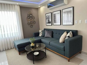 A modern living room with a sectional sofa, a glass coffee table, and framed pictures on the wall. - Serene 2-bedroom Apartment With Mountain Views in Santiago (Santiago de los Caballeros)