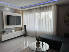 A modern living room with a flat-screen TV, a glass coffee table, a sofa, and a radiator. - Serene 2-bedroom Apartment With Mountain Views in Santiago (Santiago de los Caballeros)