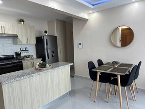 A modern kitchen with a central island, a dining area with a glass table, and a round mirror on the wall. - Serene 2-bedroom Apartment With Mountain Views in Santiago (Santiago de los Caballeros)