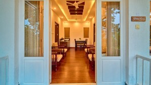 A hotel entrance with a wooden floor, a dining area with chairs and a table, and a ceiling fan. - Mistaura Home By Voye Homes (Udumbanchola)