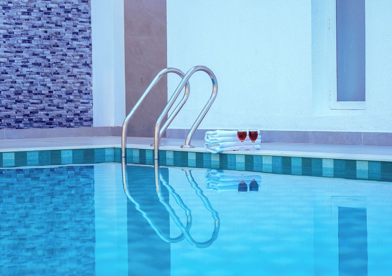 A clear swimming pool with a metal ladder, a tiled wall, and a window.