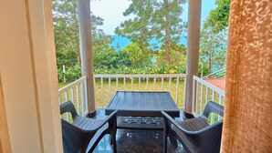 A covered outdoor seating area with a table and chairs, surrounded by a white railing, overlooking a garden and trees. - Mistaura Home By Voye Homes (Udumbanchola)