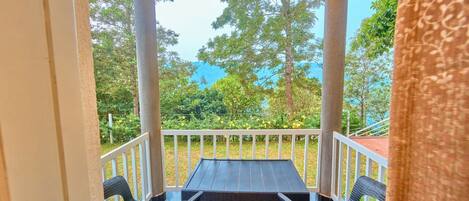 A covered outdoor seating area with a table and chairs, surrounded by a white railing, overlooking a garden and trees.