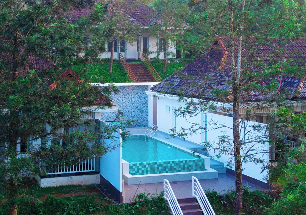A swimming pool with a tiled deck, surrounded by greenery and a staircase leading to a building.