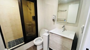 Un baño moderno con ducha envuelta en vidrio, inodoro y lavamanos con espejo superior.