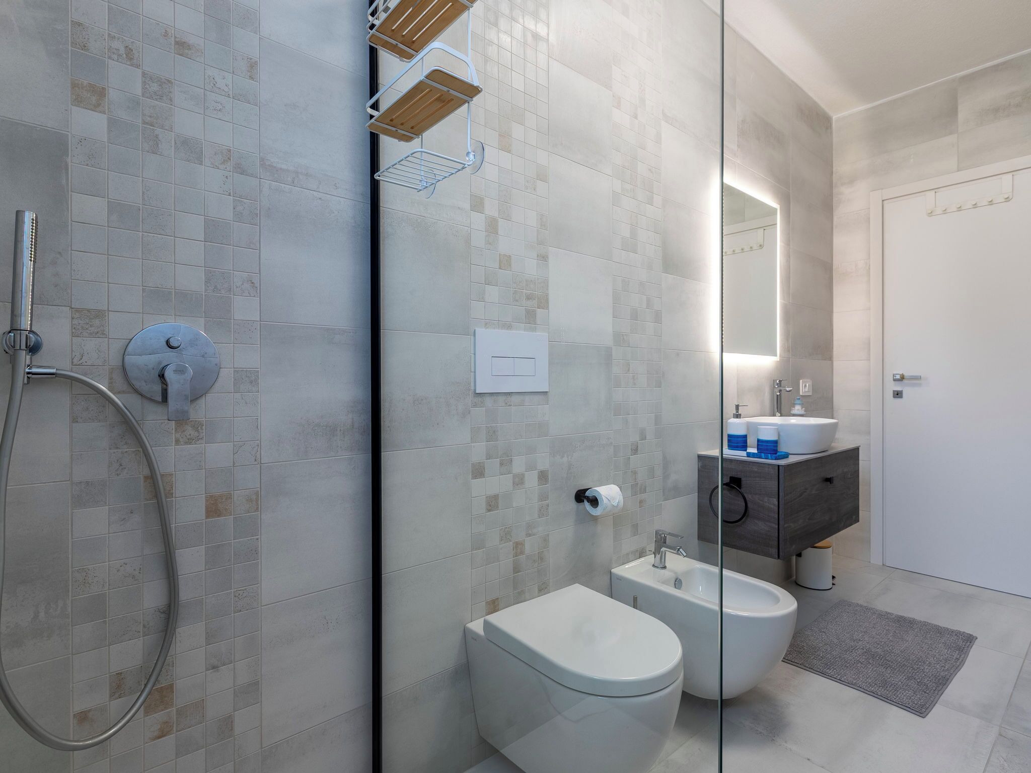 A modern bathroom with a glass shower enclosure, a toilet, bidet, and a vanity with a mirror.
