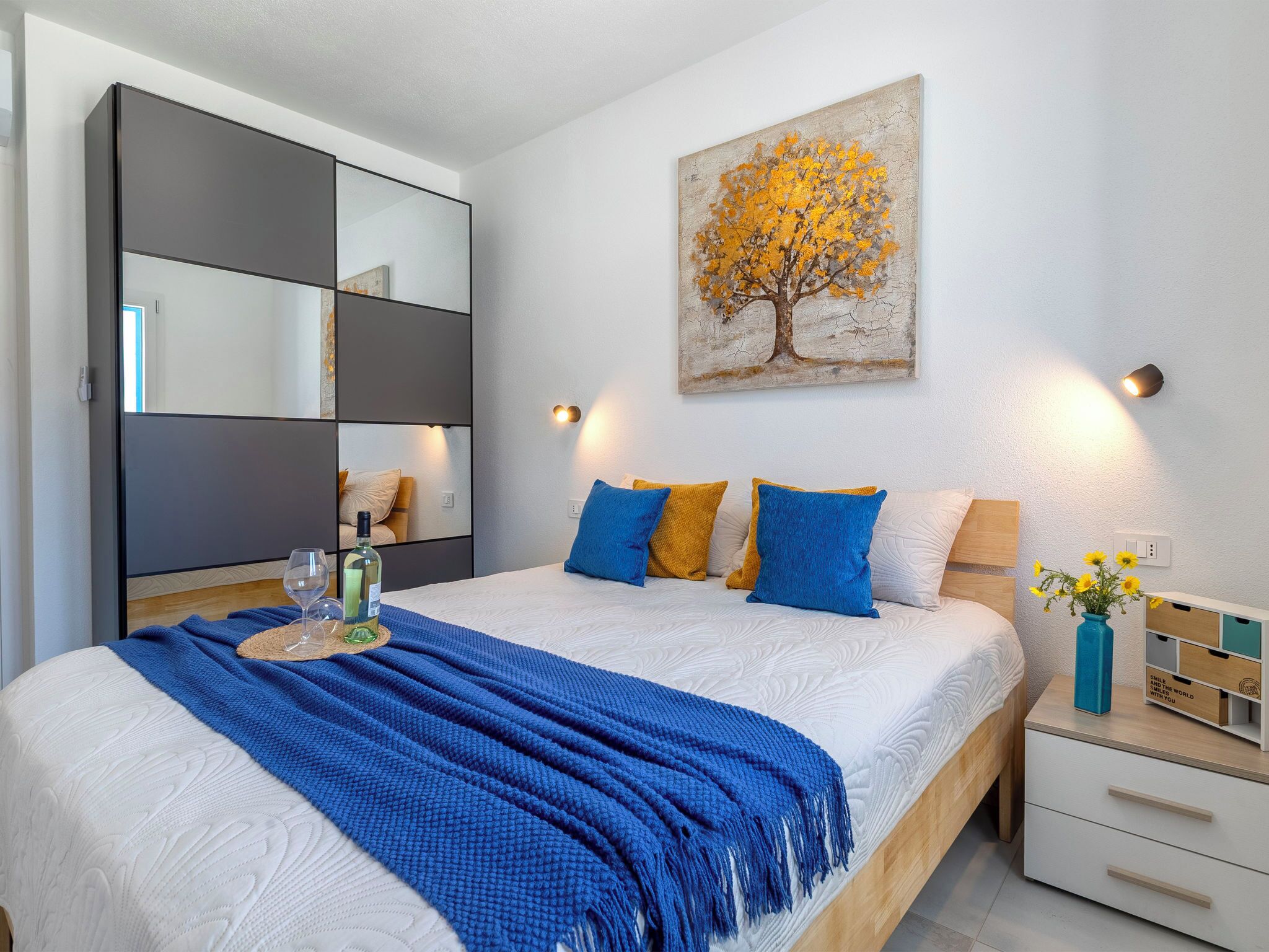 Une chambre à coucher moderne avec un lit, des tables de chevet, un miroir, un tableau et un vase de fleurs.