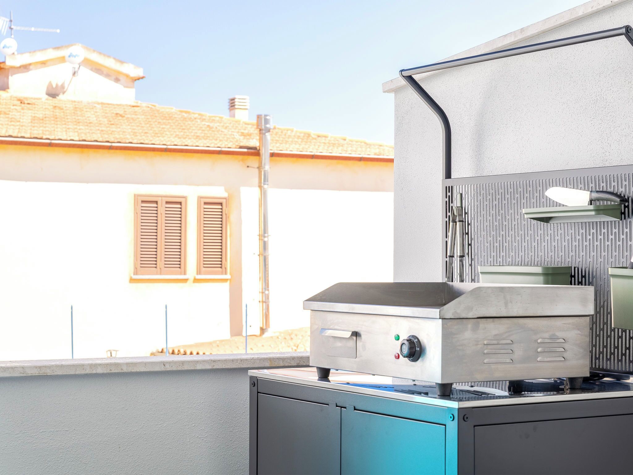 Cocina exterior con parrilla, pileta y ventana con vista a una casa.