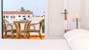 Une chambre avec un lit, une armoire blanche, une table avec des chaises et une vue sur des immeubles et des palmiers.