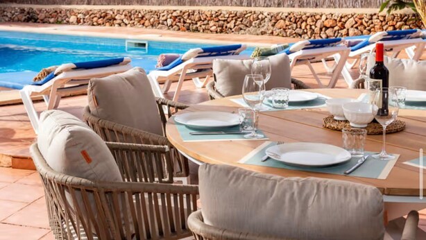 Un espace repas aménagé au bord de la piscine, avec des chaises longues, une table dressée pour deux personnes et une vue sur la piscine.