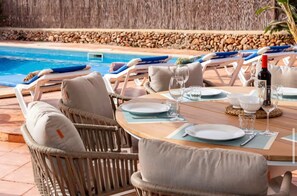 A poolside dining area with lounge chairs, a table set for two, and a view of the pool. - Villa Jultomas (Cap d'Artrutx)