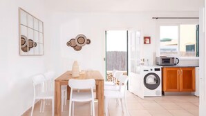 Une cuisine moderne équipée d’un lave-linge, d’une table à manger avec des chaises et donnant sur l’extérieur grâce à une porte vitrée.