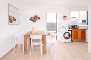 A modern kitchen with a washing machine, a dining table with chairs, and a view through a glass door.
