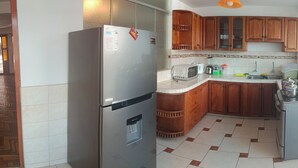 Eine Küche mit Holzausstattung, inklusive Kühlschrank, Mikrowelle, Herd und Wasserspender.