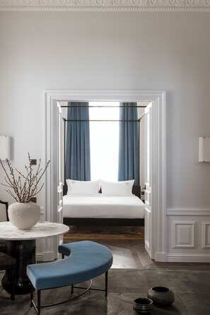 Quarto com cama, cadeira, mesa e um vaso com ramos.