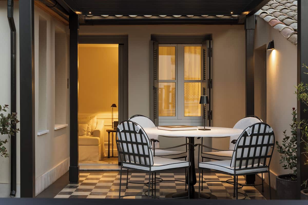Um chão xadrez, uma mesa com cadeiras e uma porta que dá para um quarto.