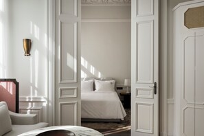 Quarto de hotel com uma cama, mesa de cabeceira, luminária e porta com detalhe decorativo.