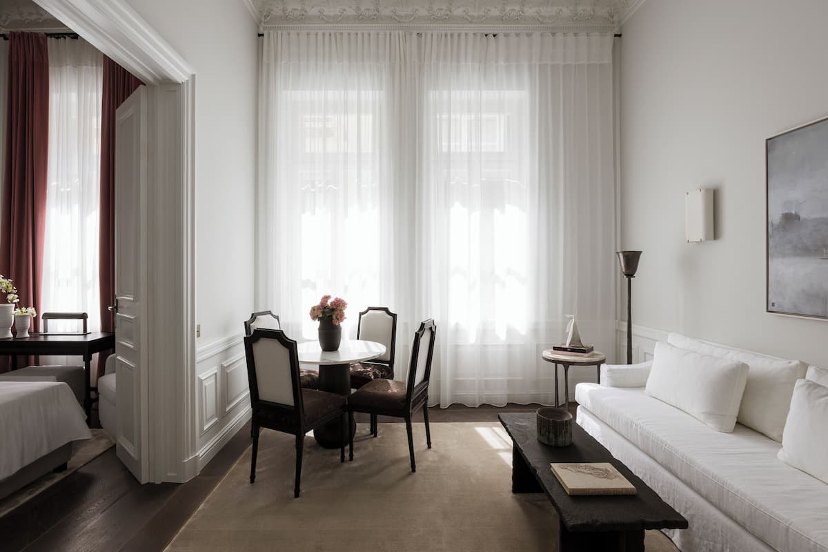 Um quarto com um sofá branco, uma mesa de jantar com cadeiras, uma mesinha de apoio e um quadro na parede.