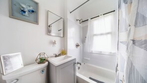 A bathroom with a toilet, sink, mirror, shower, and a window with a curtain. - 10 min to University Circle - Central Location (Cleveland)
