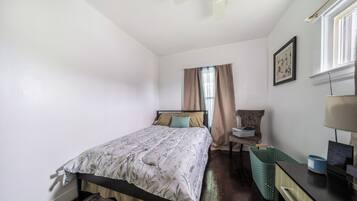 A bedroom with a bed, a chair, a desk, a lamp, a window with curtains, and a ceiling fan.