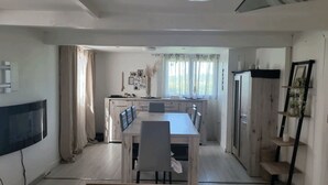 A compact kitchen with a dining table and chairs, a refrigerator, and a window with curtains. - Chalet-type house for 7 people with swimming pool near Disneyland Paris (EuroDisney) (Villiers-sur-Morin)