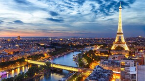Une vue urbaine avec la Tour Eiffel illuminée, une riviÚre traversée de ponts et une architecture urbaine dense.