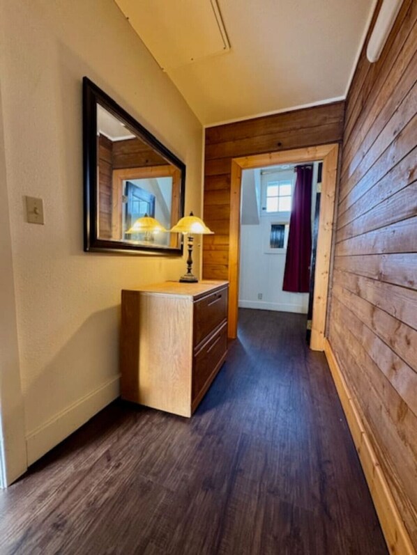 A hallway with wooden walls, a wooden dresser with a lamp, and a mirror.