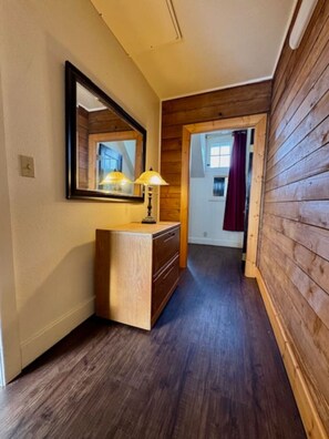 Ein Korridor mit Holzwänden, einer Holzkommode mit Lampe und einem Spiegel.