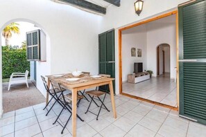 A dining area with a table and chairs, a small seating area with a bench, and a view into a room with a television and a plant. - Villa Gumm (Cap d'Artrutx)