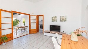 Ein modernes Wohnzimmer mit Fernseher, Esstisch aus Holz und Schiebetüren, die auf einen Balkon führen.