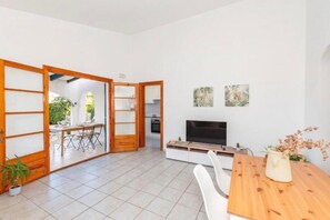 Una sala moderna con televisor, mesa de comedor de madera y puertas correderas que dan a un balcón.