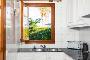 Una cocina con ventana, un lavamanos, un tostador y una tetera.