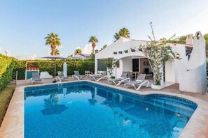 Un área de piscina moderna con sillones, piscina y un edificio de diseño arquitectónico único.