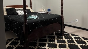 Ein Himmelsbett mit einer schwarz-weißen Bettdecke, ein blauer Ventilator und eine weiße Wand mit Deckenlüftung.