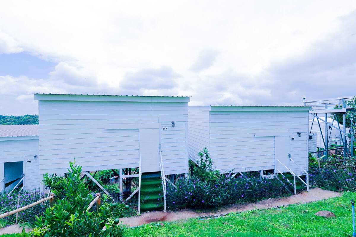 Fileira de casas móveis brancas com escadas externas, rodeadas por vegetação.