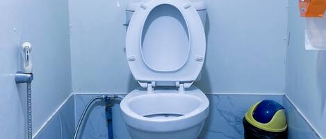 A bathroom with a white toilet, a shower, and a trash bin.