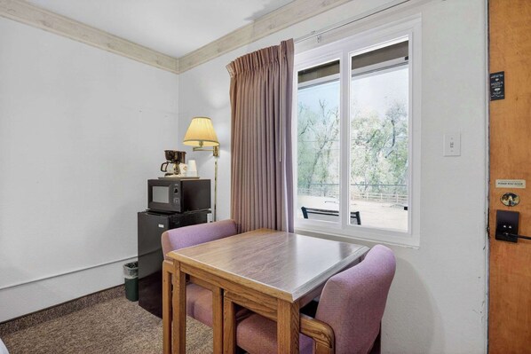 Une pièce avec une table en bois, des chaises violettes, un téléviseur, une lampe et une fenêtre avec des rideaux.
