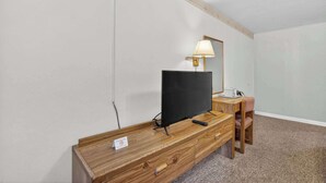 A room with a wooden TV stand, a flat-screen TV, a lamp, a desk, and a chair. - Eagle Motel Suite 112 (Manitou Springs)
