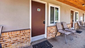 A building entrance with a brown door, a brick wall, and a covered porch area with metal chairs. - Eagle Motel Suite 112 (Manitou Springs)