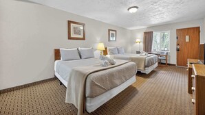 A hotel room with two beds, a desk, a lamp, and a window with curtains.