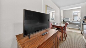 A hotel room with a flat-screen TV on a wooden dresser, a dining table with chairs, a large mirror, and a bathroom with a sink and mirror. - Eagle Motel Suite 118 (Manitou Springs)