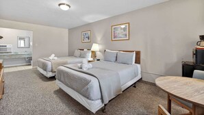 A hotel room with two beds, a desk, a chair, a small table, a lamp, and a TV. - Eagle Motel Suite 114 (Manitou Springs)