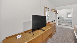 A hotel room with a TV on a wooden dresser, a mirror, a bathroom with a sink and mirror, and a bed. - Eagle Motel Suite 114 (Manitou Springs)