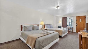 A hotel room with two beds, a desk, a chair, and a window with curtains. - Eagle Motel Suite 108 (Manitou Springs)