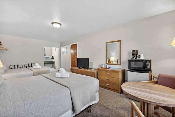 A hotel room with two beds, a television, a microwave, a wooden table, and a mirror. - Eagle Motel Suite 110 (Manitou Springs)