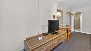 A hotel room with a wooden desk, a television, a lamp, a shower, and a door. - Eagle Motel Suite 106 (Manitou Springs)