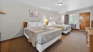 Quarto de hotel com duas camas, uma escrivaninha, uma cadeira, um armário e uma porta que dá para o exterior.