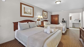 A hotel room with two beds, a wooden headboard, a nightstand with a lamp, a wardrobe, and a bathroom visible through an open door. - Eagle Motel Suite 117 (Manitou Springs)
